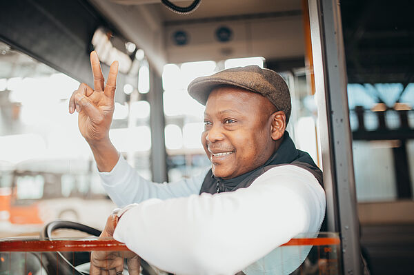 Berufskraftfahrer sitzt am Steuer eines Linienbusses und winkt aus dem Fenster nach vorn