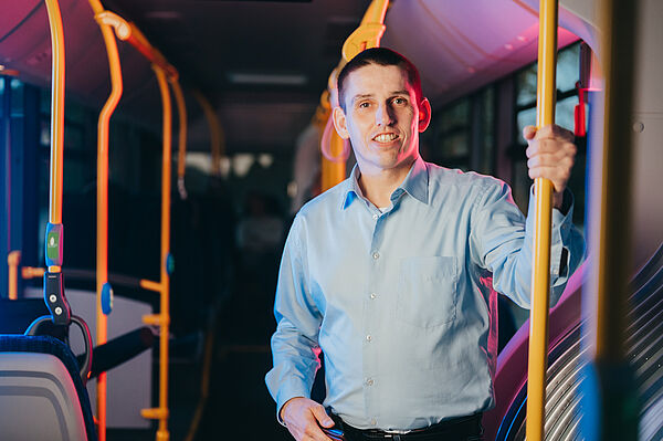 Fahrgast steht im Bus und hält sich fest, es ist dunkel draußen. 
