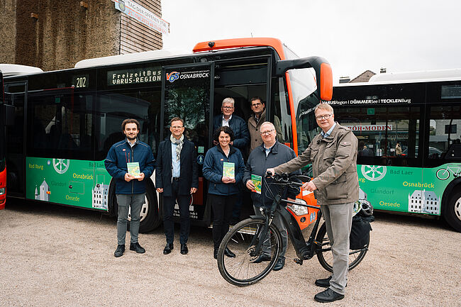 Personen vor dem FreizeitBus mit neuer Beklebung und Slogan beim Pressetermin, eine Person mit Fahrrad.