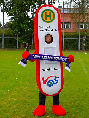 Das V O S Maskottchen – Haltelinchen ist auf einem Fußballfeld und hält ein V F L - Schal hoch