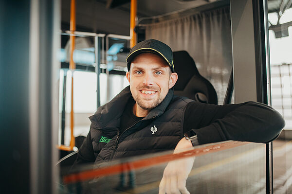 Busfahrer sitzt am Steuer eines Busses und lächelt aus dem Seitenfenster