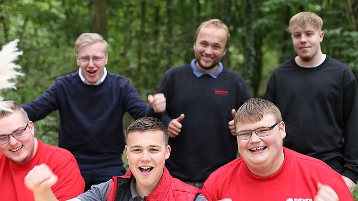 Sechs Azubis der V O S lachen gemeinsam in die Kamera und jubeln.