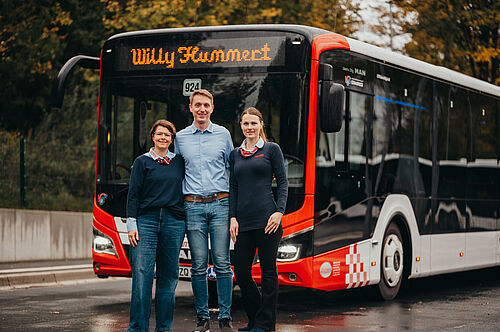 Drei Mitarbeitende stehen vor einem Linienbus und halten sich in den Armen.