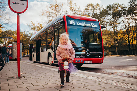 Ein Grundschulkind spielt vor dem Bus mit ihrem Steckenpferd und lächelt.