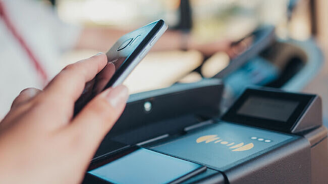 Hand hält Smartphone über ein Digitales Lesegerät im Bus.