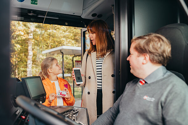 Mutter mit Tochter zeigen ihre Buskarten vor, sowohl digital als auch physisch.