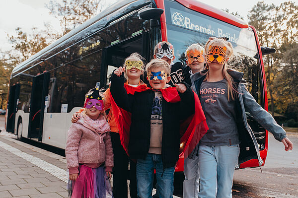 Eine Gruppe von verkleideten Kinder stehen vor dem Bus. 