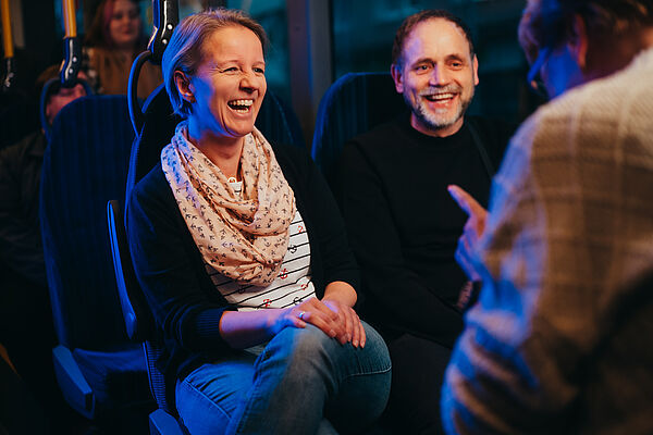 Zwei lachende Fahrgäste sitzen nachts im Bus und unterhalten sich. 