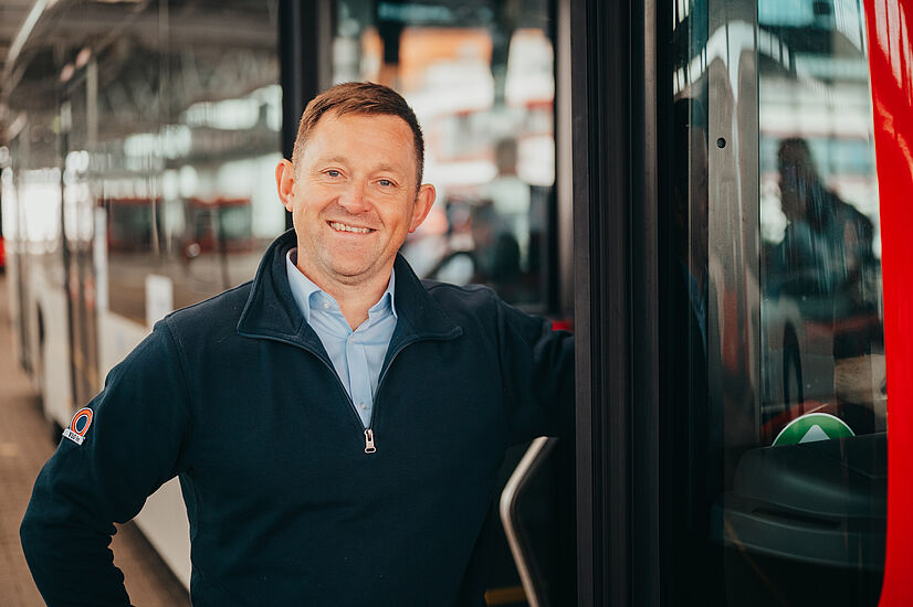Busfahrer steht neben der Tür zum Bus und lächelt. 