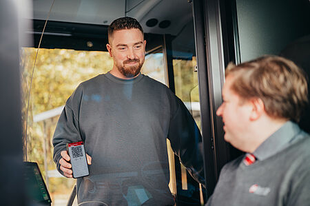 Ein Mann zeigt dem Busfahrer im Bus seine digitale Fahrkarte auf dem Handy.