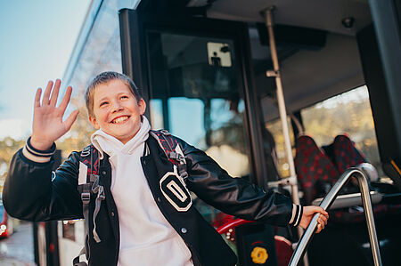 Ein Junge steigt in einen Bus ein und winkt zurück. 