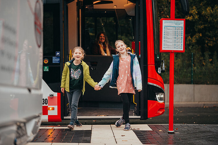 Zwei Kinder steigen aus dem Bus aus und halten sich an den Händen fest.