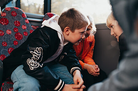 Mehrere Kinder sitzen im Bus zusammen und reden.