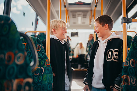Zwei Schulkinder stehen im Bus und reden miteinander.