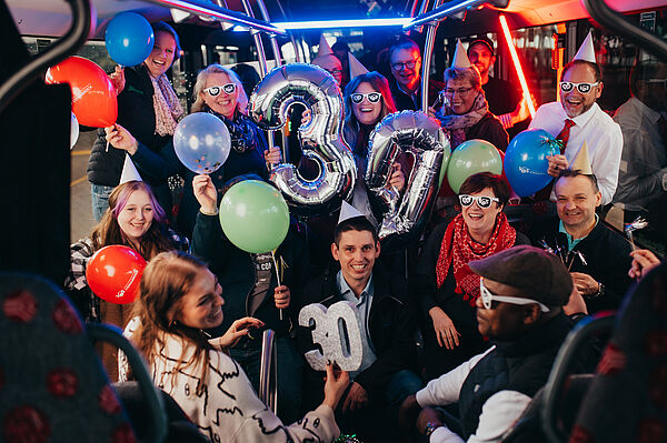Eine große Gruppe feiert im Bus aufgrund des 30-Jährigen Jubiläums der VOS. 